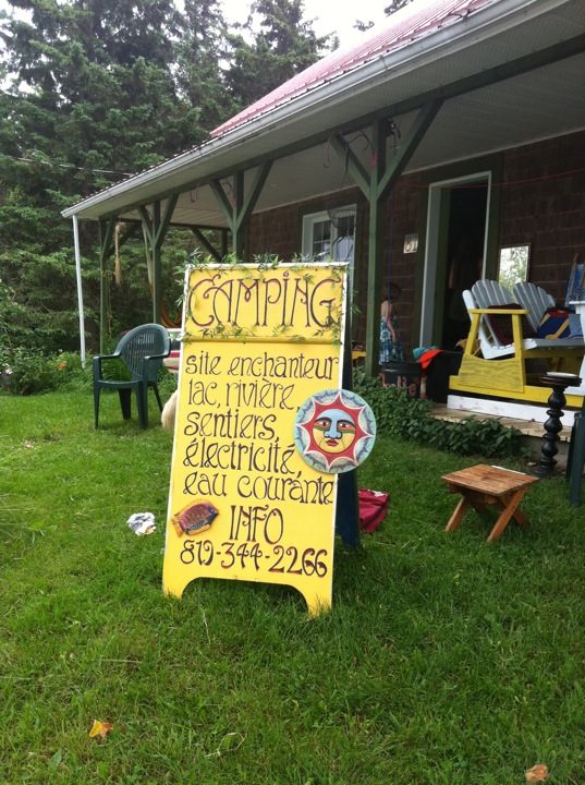 Juillet 2011 : le panneau peint à la main devant la galerie de la maison. « Camping : site enchanteur, lac, rivière, sentiers, électricité, eau courante. »